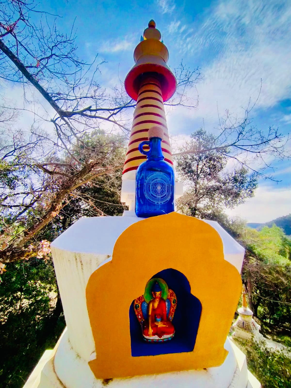 Botella Devi frente a una estupa, banderas de oración al viento